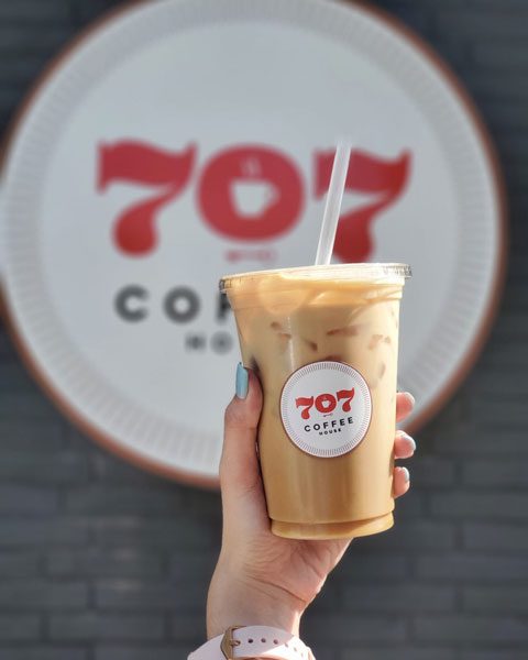 Young person hand holding an iced coffee from a store opening up business in Alamo.